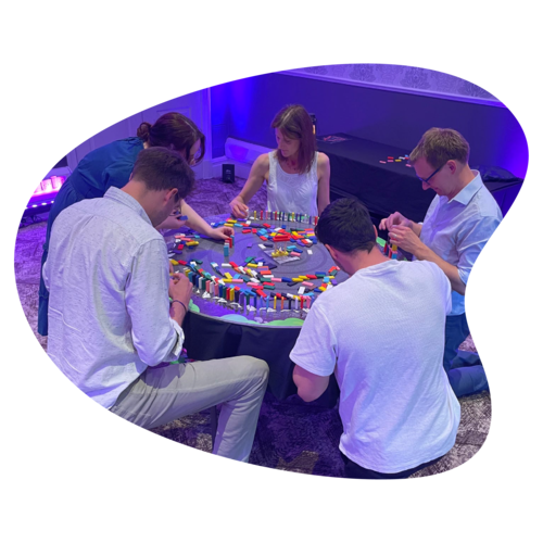 A group of five people are gathered around a table, stacking dominoes. A group of five people are gathered around a table, stacking dominoes.
